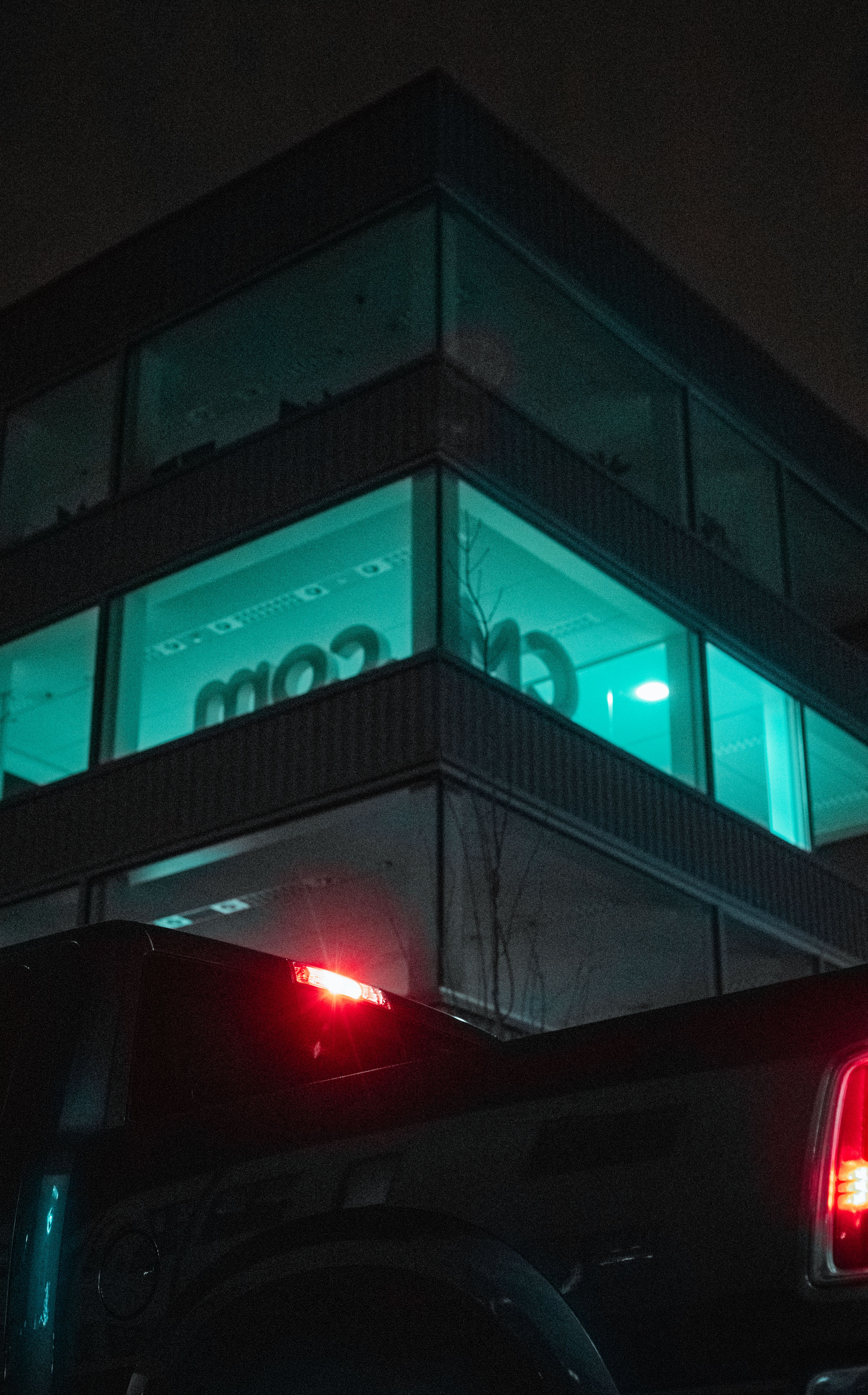 Illuminated modern office building facade at night with a red-taillight pickup truck in Breda, Netherlands.
