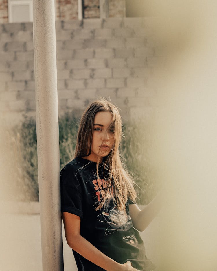 Serious Woman With Long Flying Hair Leaning On Metal Post