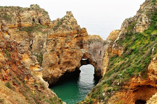 Free A breathtaking view of a natural rock arch along a rugged coastline with clear blue waters. Stock Photo