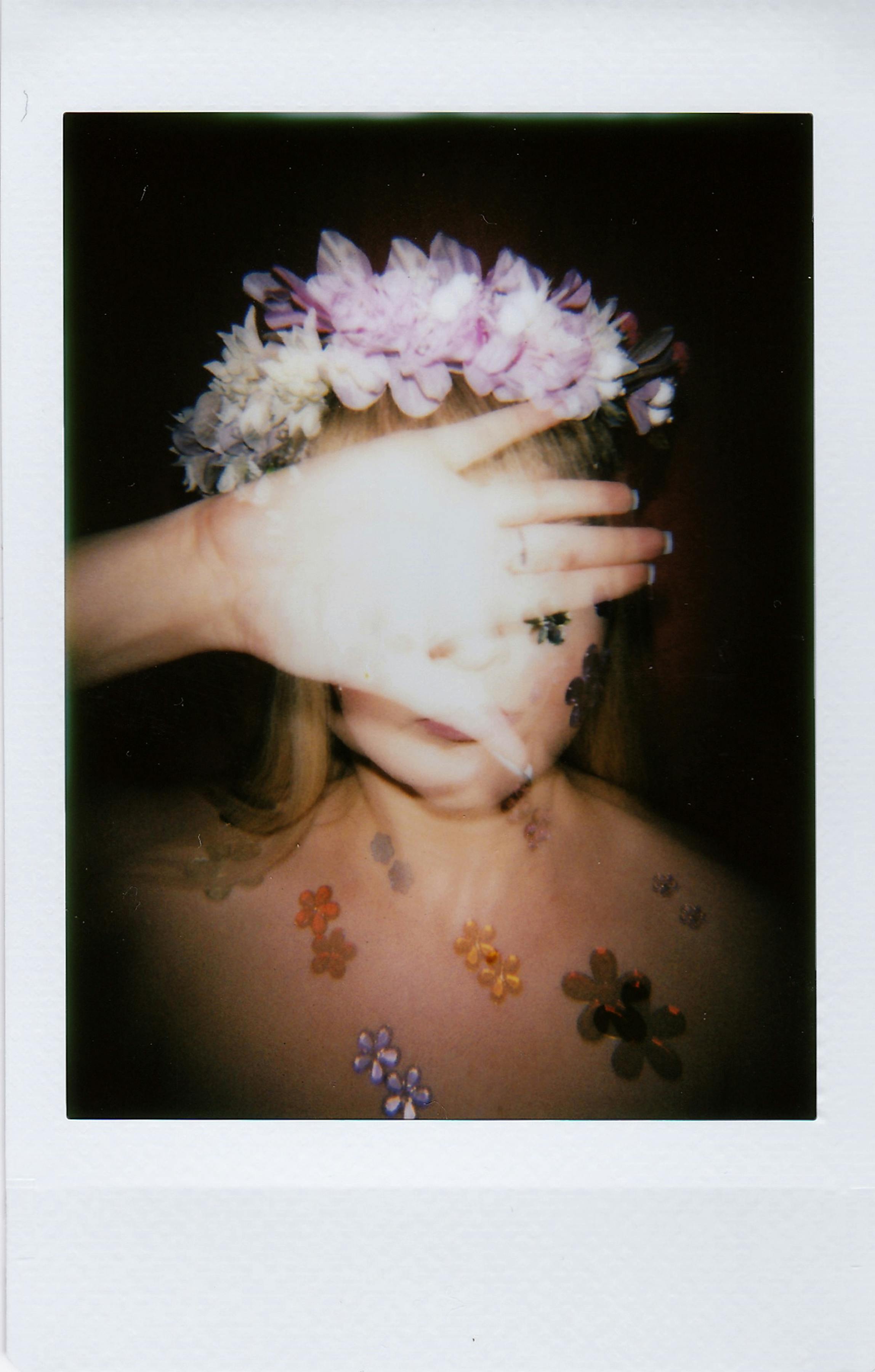 Creative portrait of a woman with floral wreath and obscured face, showcasing vibrant flowers.