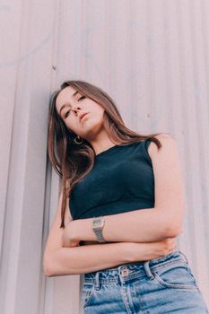 Low angle of upset female with crossed hands leaning on metal wall and looking at camera