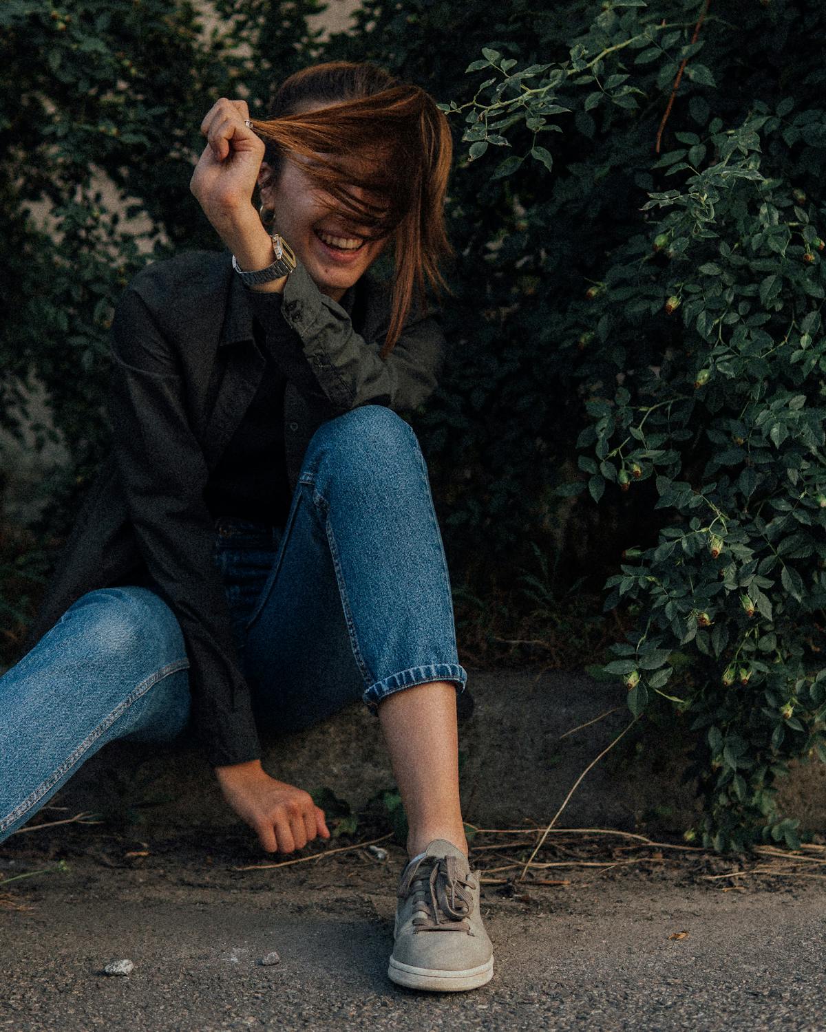 Young woman laughing while sitting on curb · Free Stock Photo
