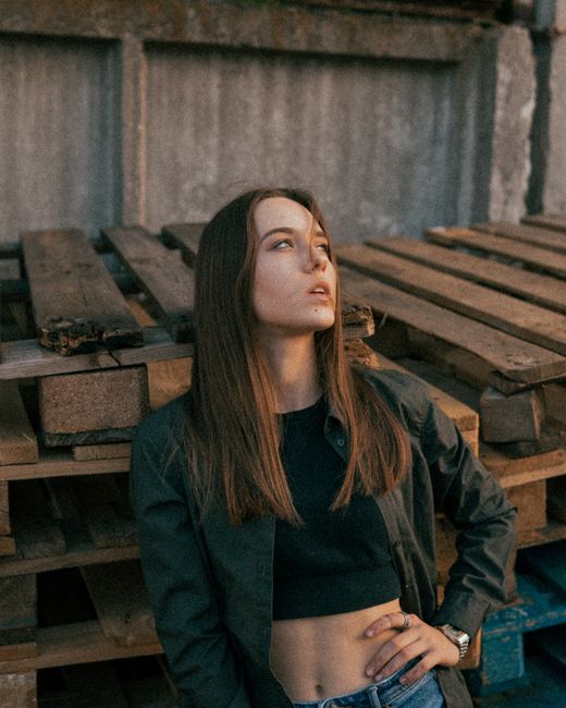 High angle of confident young female with long hair wearing casual clothes with bare tummy standing near wooden pallets