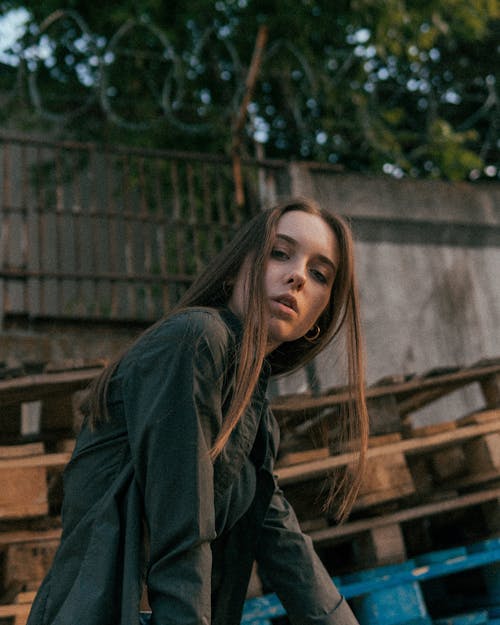 Low angle side view of charismatic female with long hair wearing casual clothes near wooden pallets
