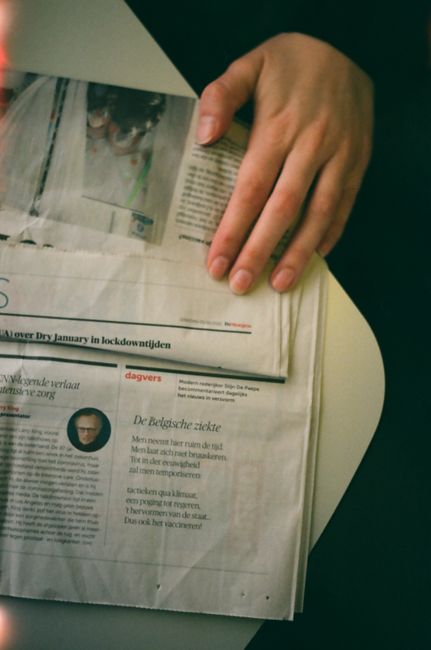 A close-up view of a hand holding a newspaper with articles in Dutch, captured indoors.