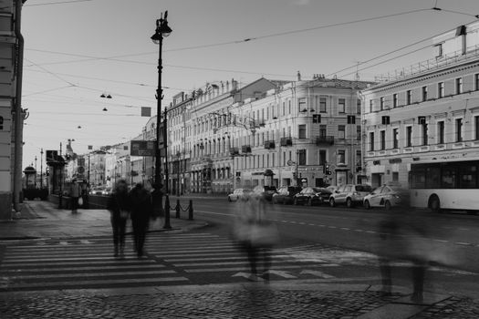 Black and white of faceless people on crosswalk and pavement in city district near asphalt road with vehicles near old buildings in daylight