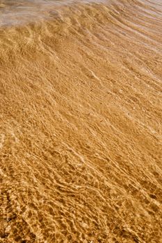 High angle of sandy wet coast near wavy rippling ocean water washing surface in summer sunny day
