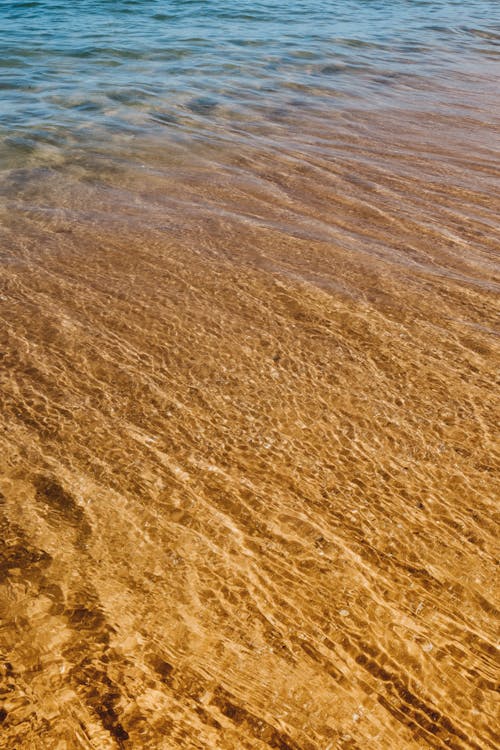 High angle of sandy wet shore near rippling seawater washing surface in summer sunny day