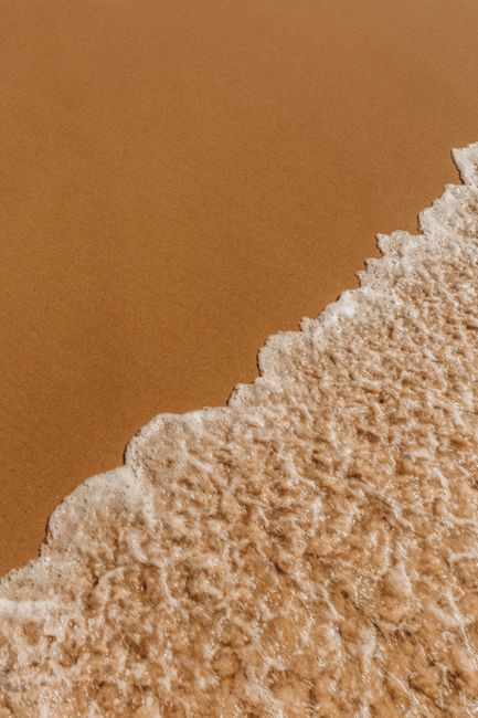 High angle of wet sandy shore near foamy wavy sea in summer day