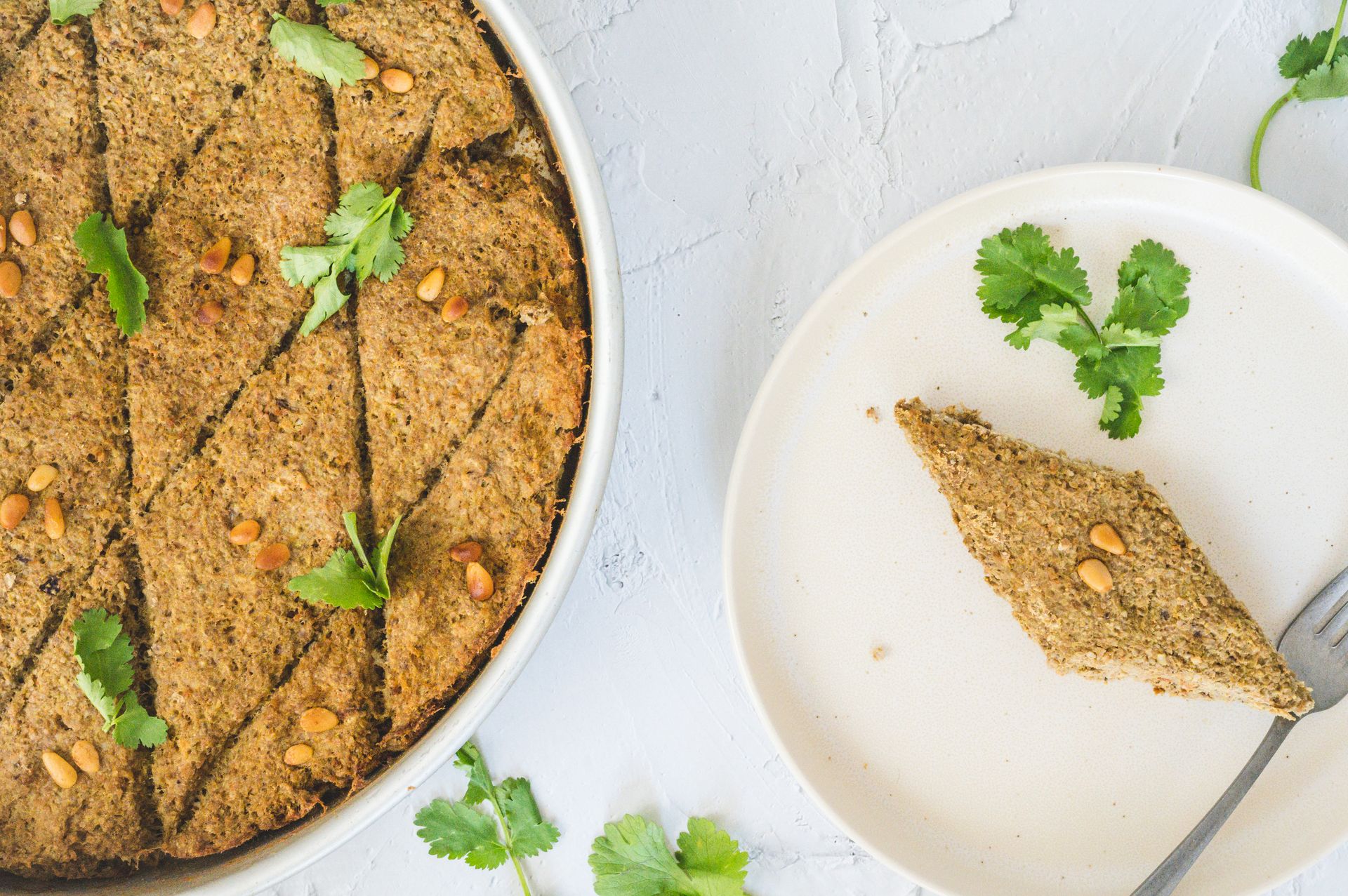 A plate of traditional baked kibbeh garnished with pine nuts and cilantro.