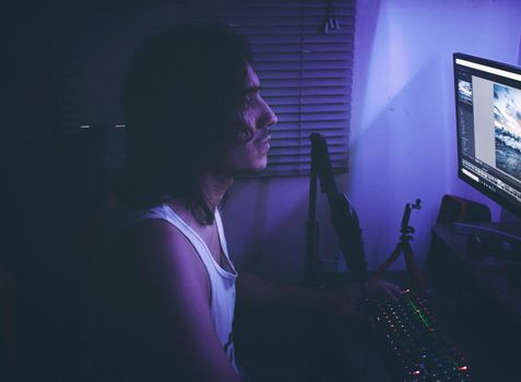 Side profile of a man at a computer in a dimly lit room with purple lighting.