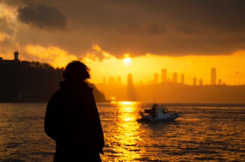 Silhouette of a Man Standing near a Body of Water during Sunset