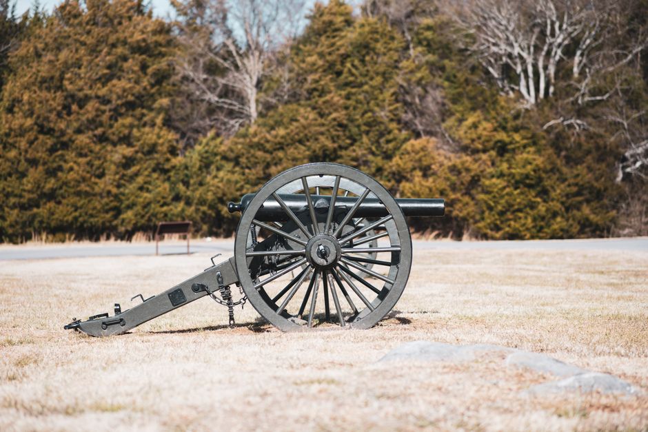 A historic cannon sits on grassy field under daylight, surrounded by trees.