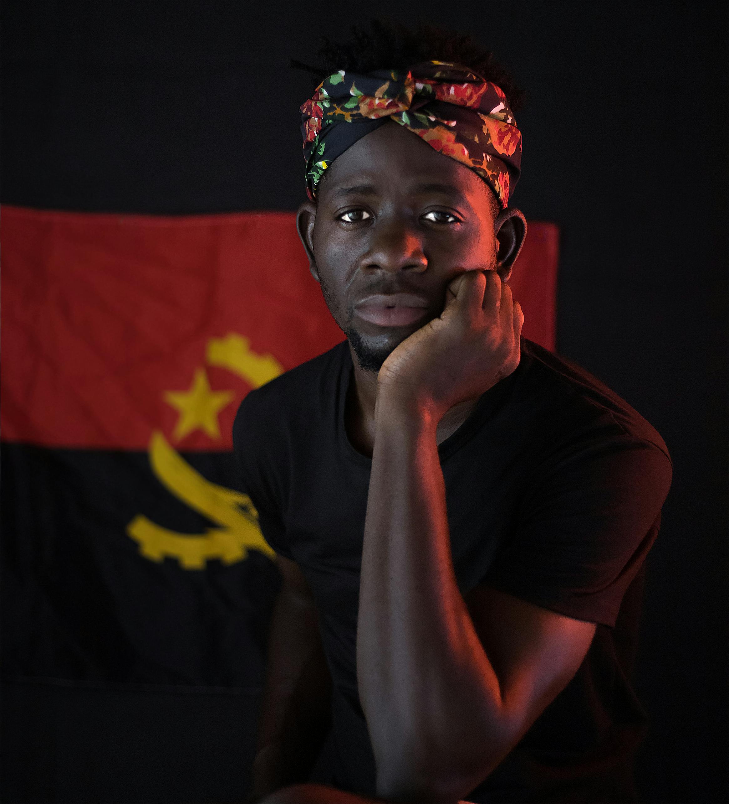 Man posing with a thoughtful expression in front of an Angolan flag, Luanda, Angola.