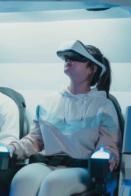 Free A Woman in White Hoodie Sitting on a Chair while Wearing VR Glasses Stock Photo
