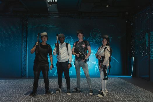 A diverse group of friends playing with VR headsets and guns in a gaming arena.