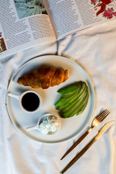 A fresh and healthy croissant breakfast with avocado, cream cheese, and coffee.