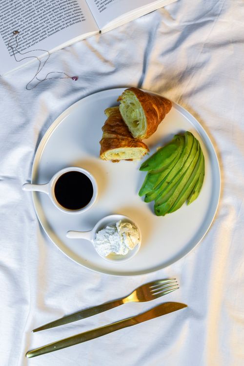 Free Flat lay of a gourmet breakfast with avocado slices, croissant, and coffee on a white plate. Stock Photo