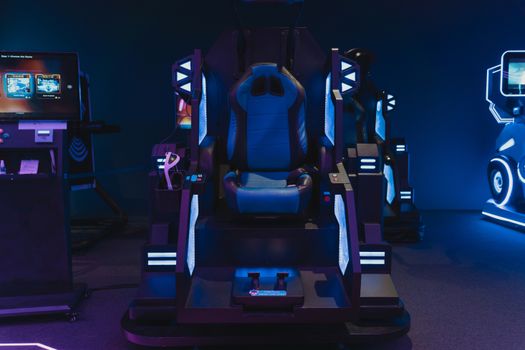 High-tech gaming simulator chair in an indoor arcade setting with neon lights.