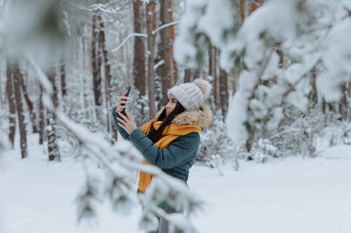 Woman in Blue Jacket and White Beanie Standing on Snow Covered Ground