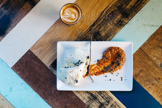Burrito with sauce and coffee on a colorful wooden table, viewed from above.