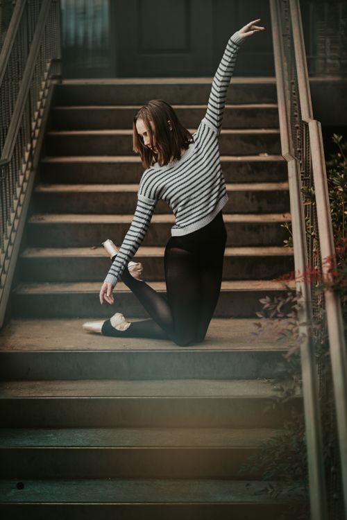 Free Full body fit pretty female dancer in leggings and pointe shoes standing on knees on stairway and raising arm gracefully Stock Photo