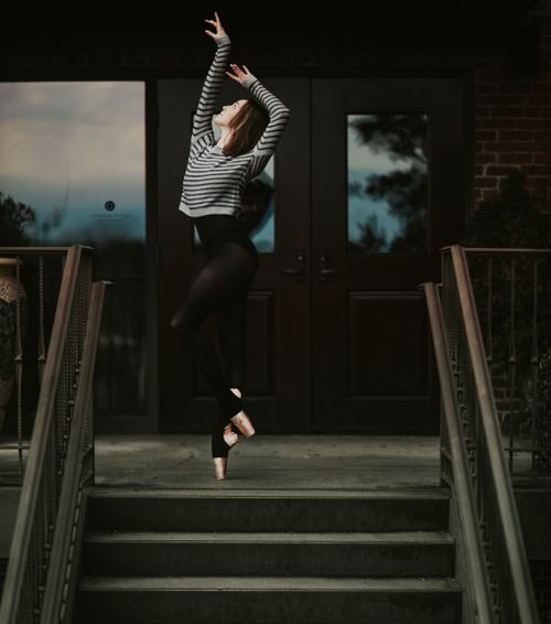 Free Full length feminine slender female dancer in leggings and pointe shoes standing on tiptoe with arms raised graciously on doorsteps Stock Photo