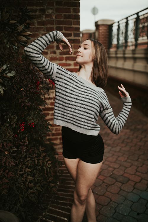 Free Positive fit female wearing shorts and casual sweater standing with arms raised graciously on paved sidewalk Stock Photo