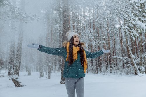 Free A happy woman with arms open enjoys the snow in a winter forest, wearing cozy attire. Stock Photo
