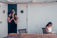 Young ladies photographing feminine bride reading letter on terrace