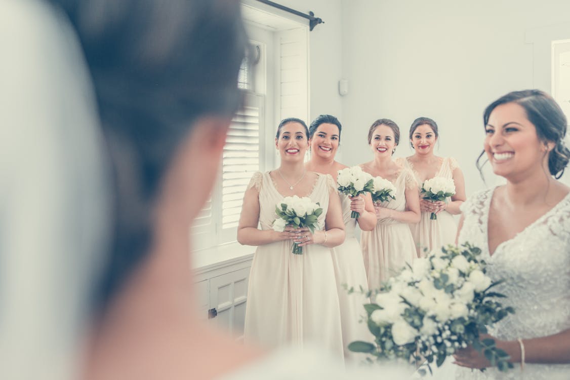Happy women wearing elegant dresses standing with bouquets of flowers while congratulating unrecognizable blurred bride in veil during wedding ceremony