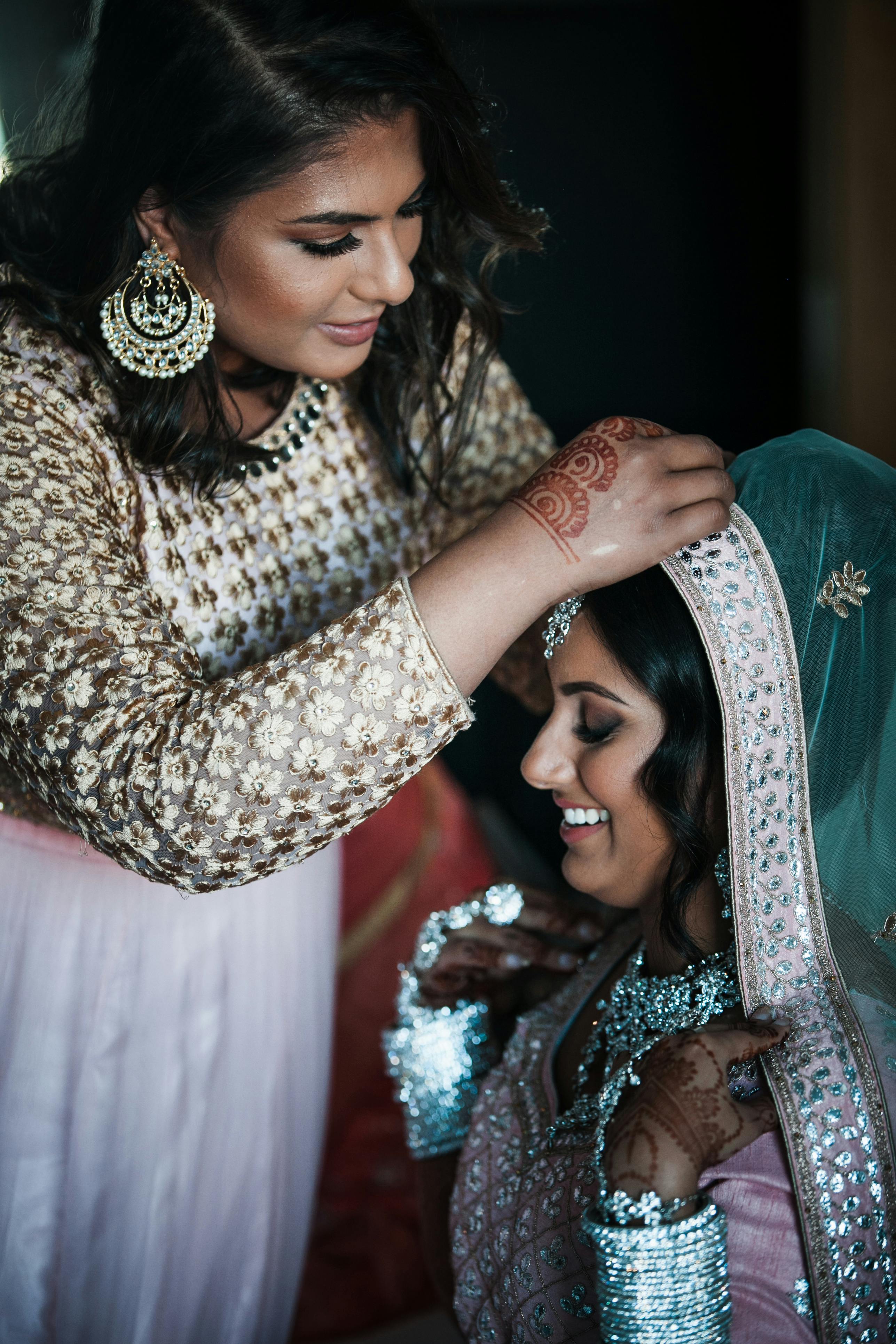 Woman helping Indian bride to get ready for wedding