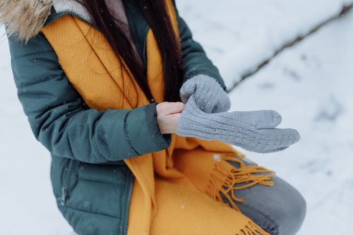 Free Close-up of a woman in a winter coat and scarf adjusting gray gloves outdoors in snow. Stock Photo