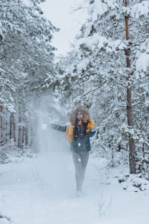 Free A woman in a winter jacket is joyfully throwing snow in a snow-covered forest. Stock Photo