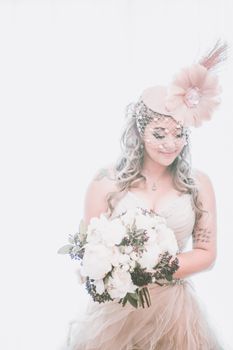 Smiling young bride in wedding dress and bridal hat with bouquet of flowers on white background