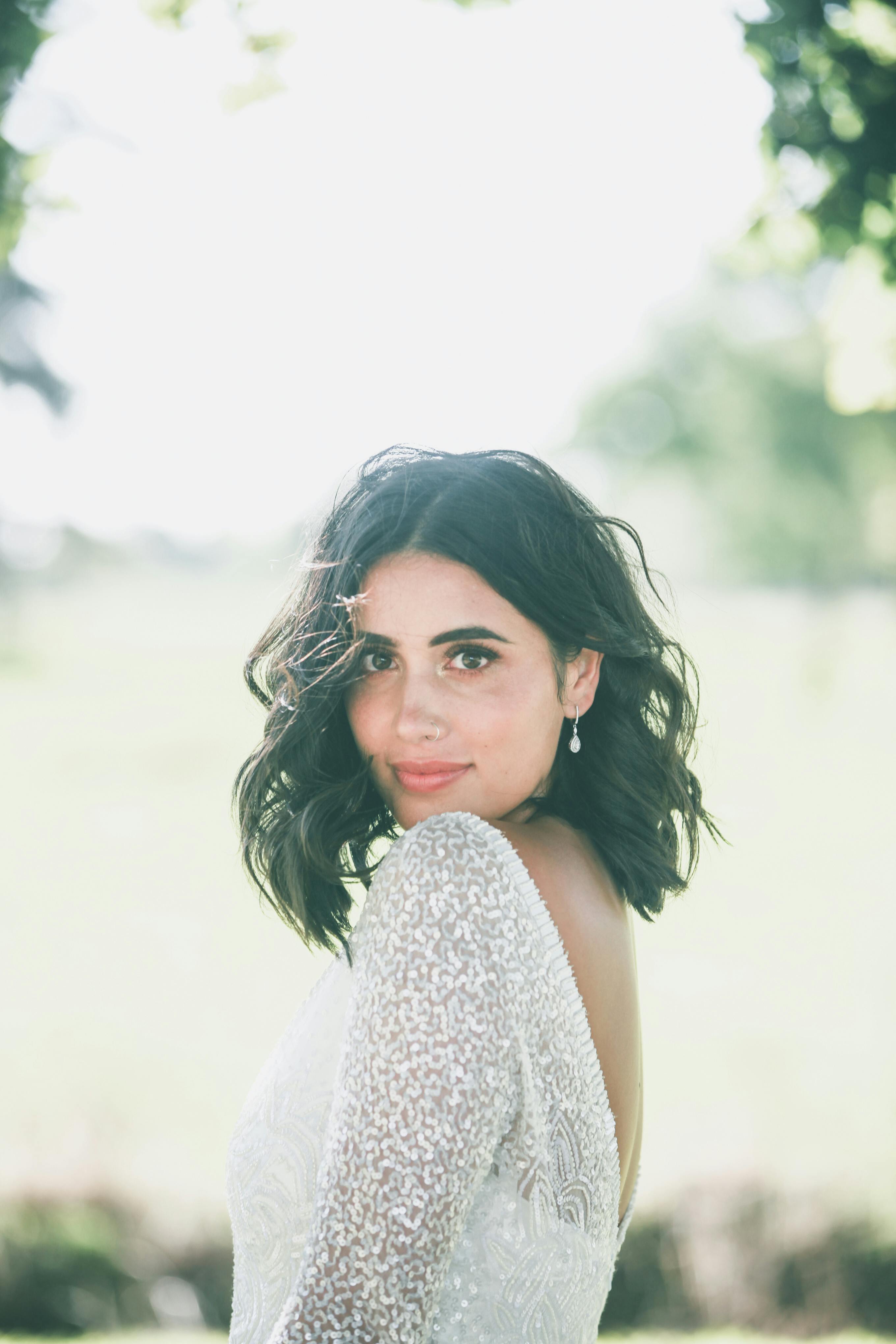 Ücretsiz Şık Elbiseli Büyüleyici Kadın Parkta Duruyor Ve Kameraya Bakıyor Stok Fotoğraflar