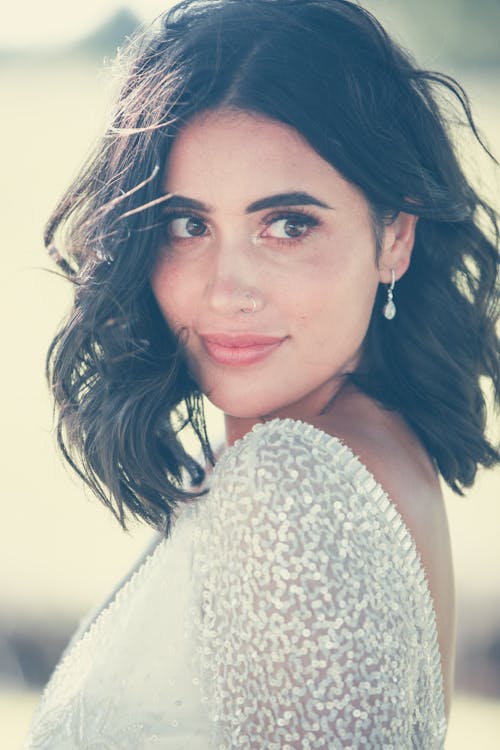 Calm woman with short dark hair in elegant white outfit and earring looking away in daylight