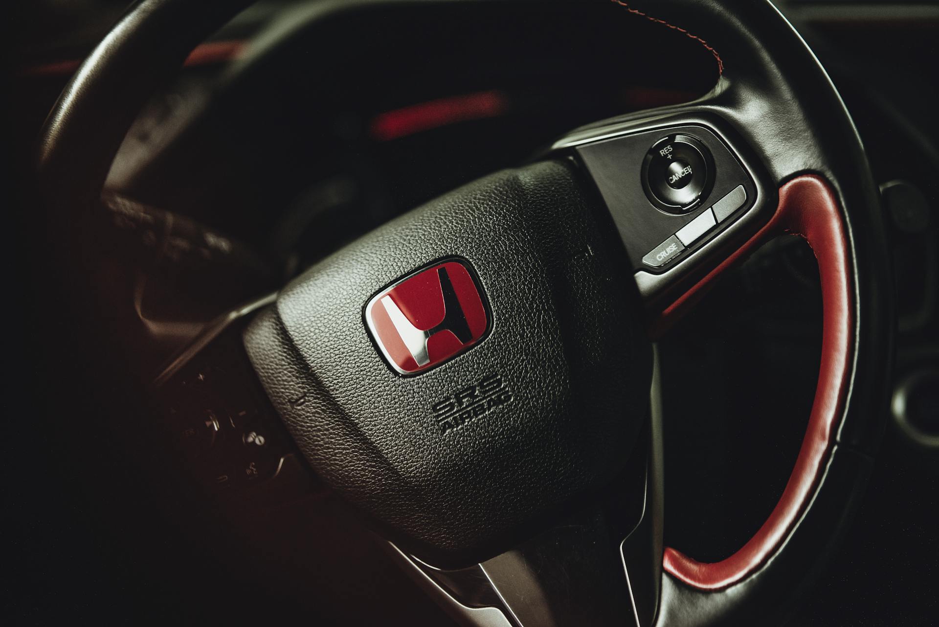 Detailed view of a sleek car's steering wheel showcasing the distinct red logo emblem.