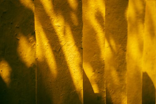 Free Abstract shadows and sunlight create patterns on a yellow textured wall. Stock Photo