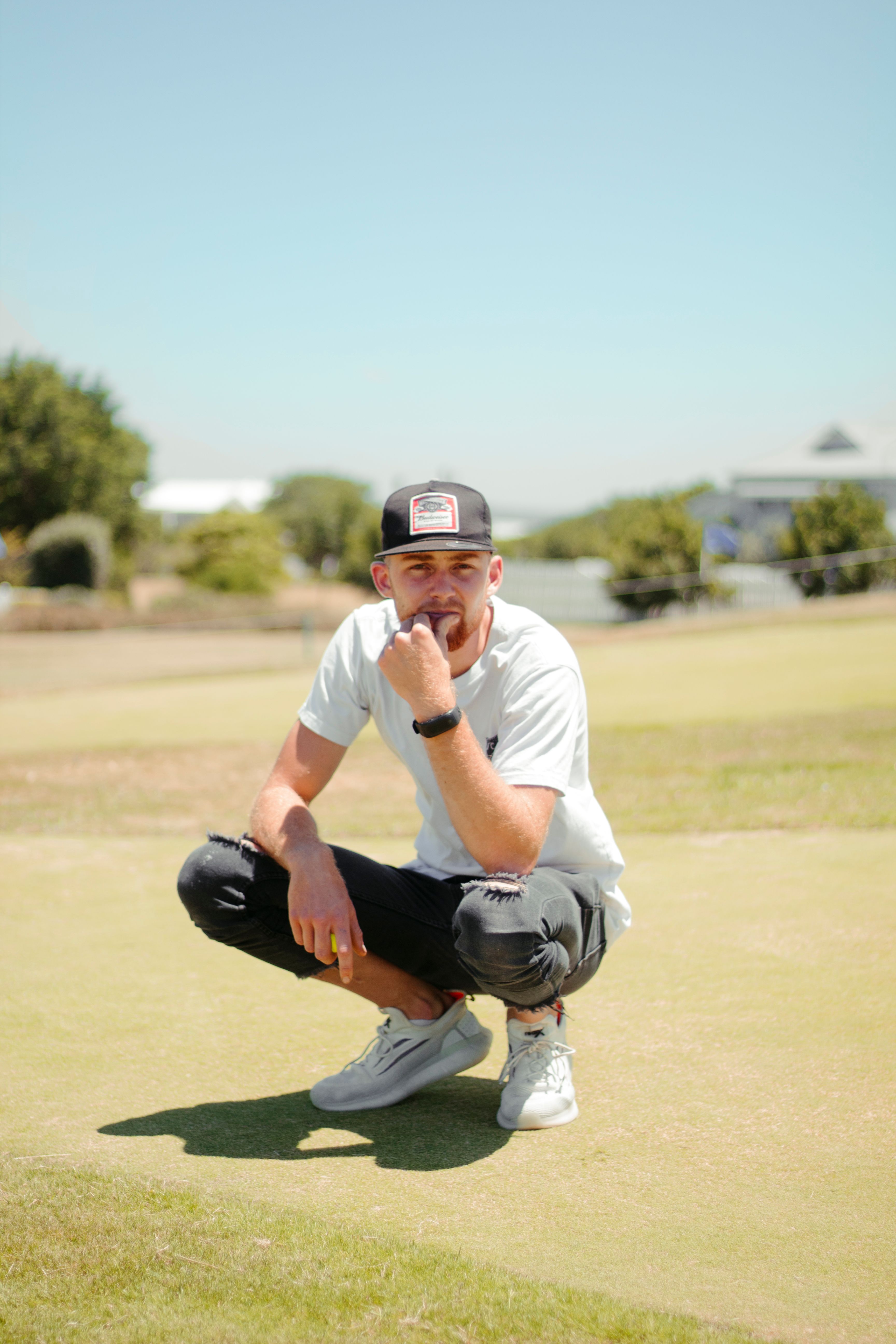 Full body of focused male touching chin sitting on grassy ground in sunny park
