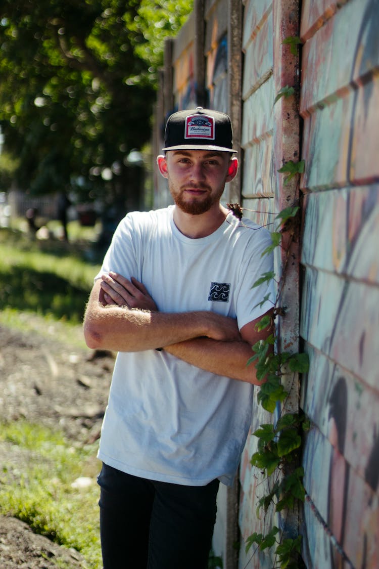 Young Bearded Man In Cap Leaning On Painted Wall