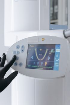Gloved hand using dental x-ray machine panel in clinic setting.