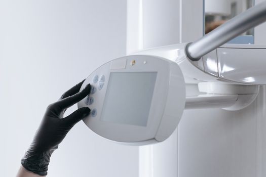 Close-up of gloved hand operating dental x-ray machine in clinical setting.