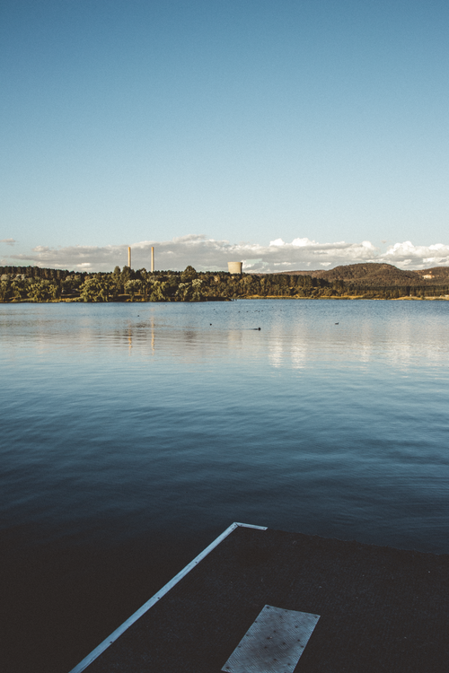 Free Serene landscape of a lake from a dock with distant hills under a clear evening sky. Stock Photo