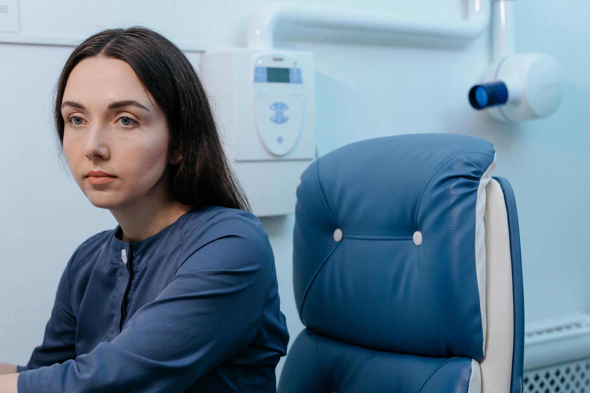 A thoughtful woman sitting in a blue chair, set in a medical clinic environment.