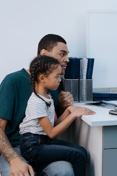 Father and daughter sitting together, engaged with a computer at home, illustrating family bonding.