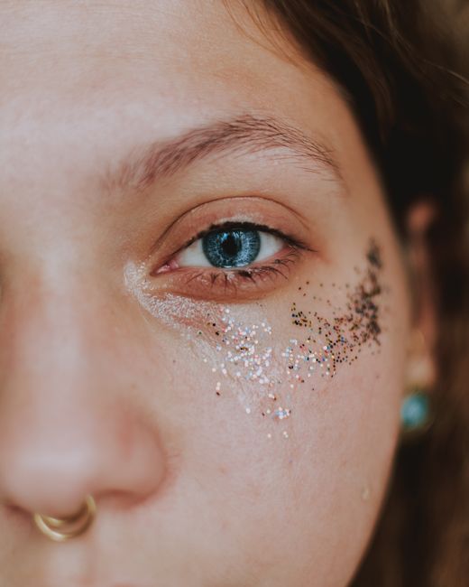 Closeup of crop anonymous young female with piercing and shiny glitters on face looking at camera in daylight