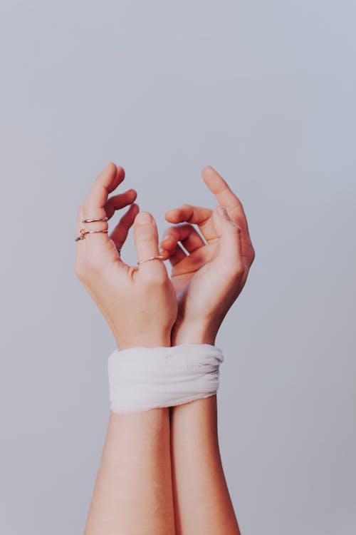 Crop faceless female with stylish rings on fingers and hands tied with white bandage against gray background