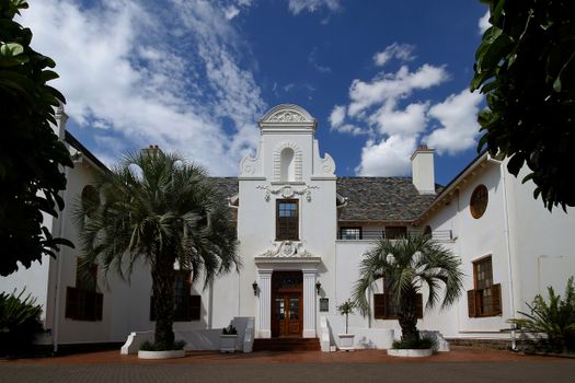 Elegant white building facade against a vibrant blue sky, featuring palm trees and classic architecture.