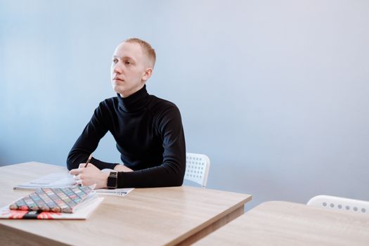 Young man in a black turtleneck writing at a desk, contemplating ideas.